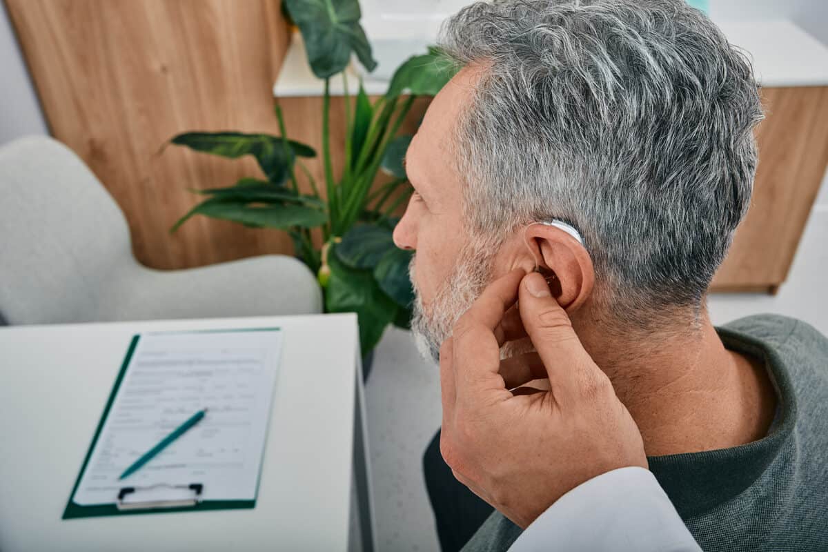 Doctor fitting hearing aid on elderly man